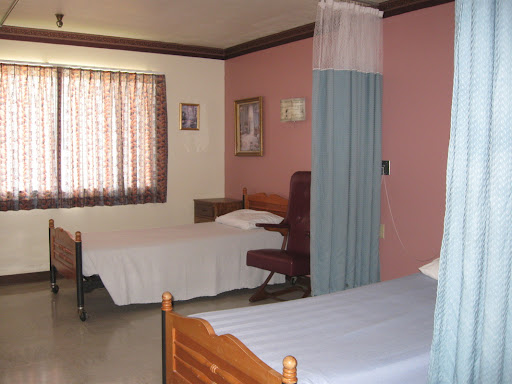 A view of a hospital patient room featuring two beds and a warm color palette.