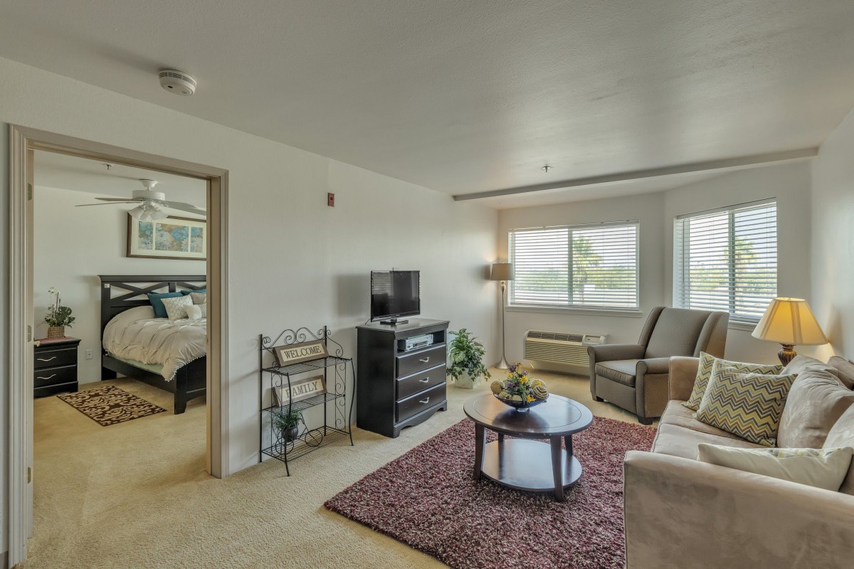 A cozy living room with comfortable seating, a television, and natural light from a large window.