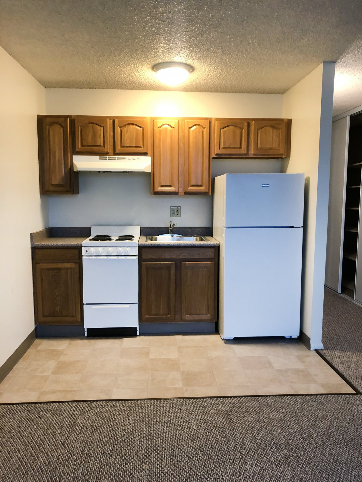 Compact apartment kitchen with wooden cabinets and white appliances.