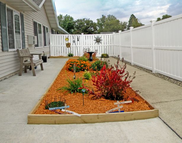 A well-maintained garden with colorful flowers and mulch next to a patio, enclosed by a white fence.