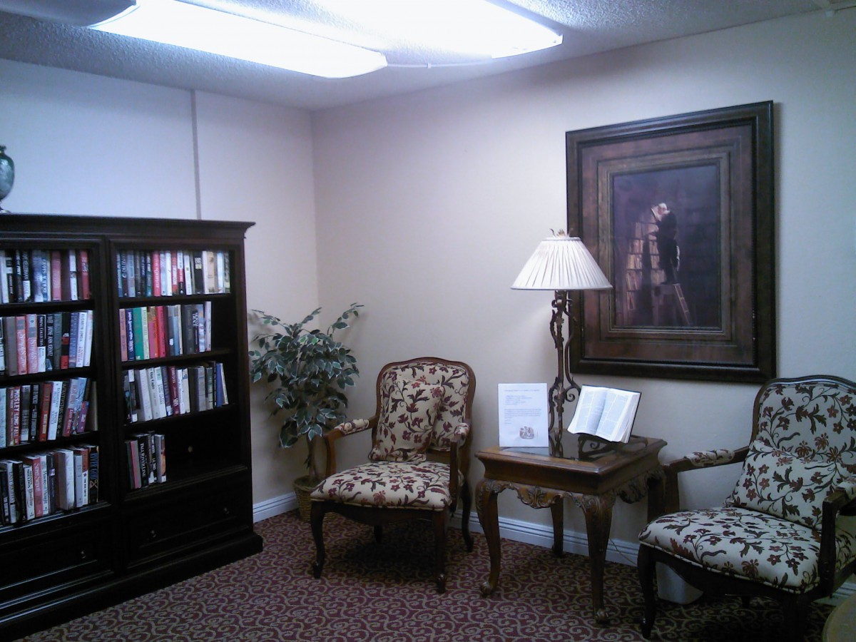 A cozy waiting room with a bookshelf, chairs, and a lamp.