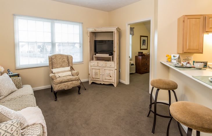 A cozy living room with a television, armchair, and stools.