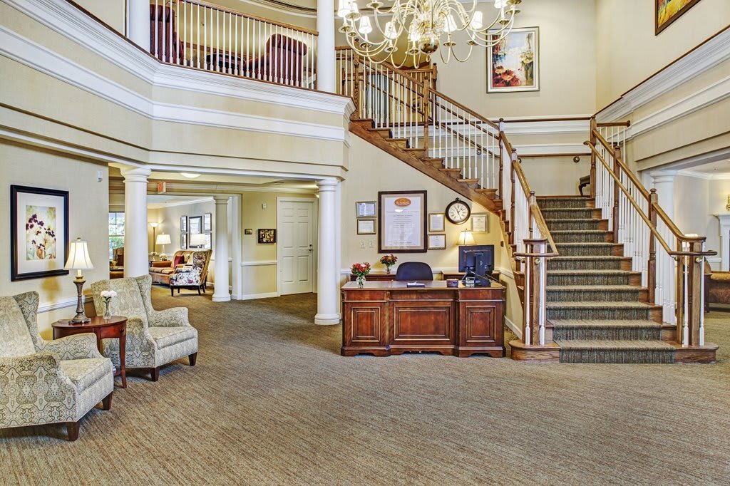 A spacious lobby featuring a grand staircase, chandelier, and a reception desk.