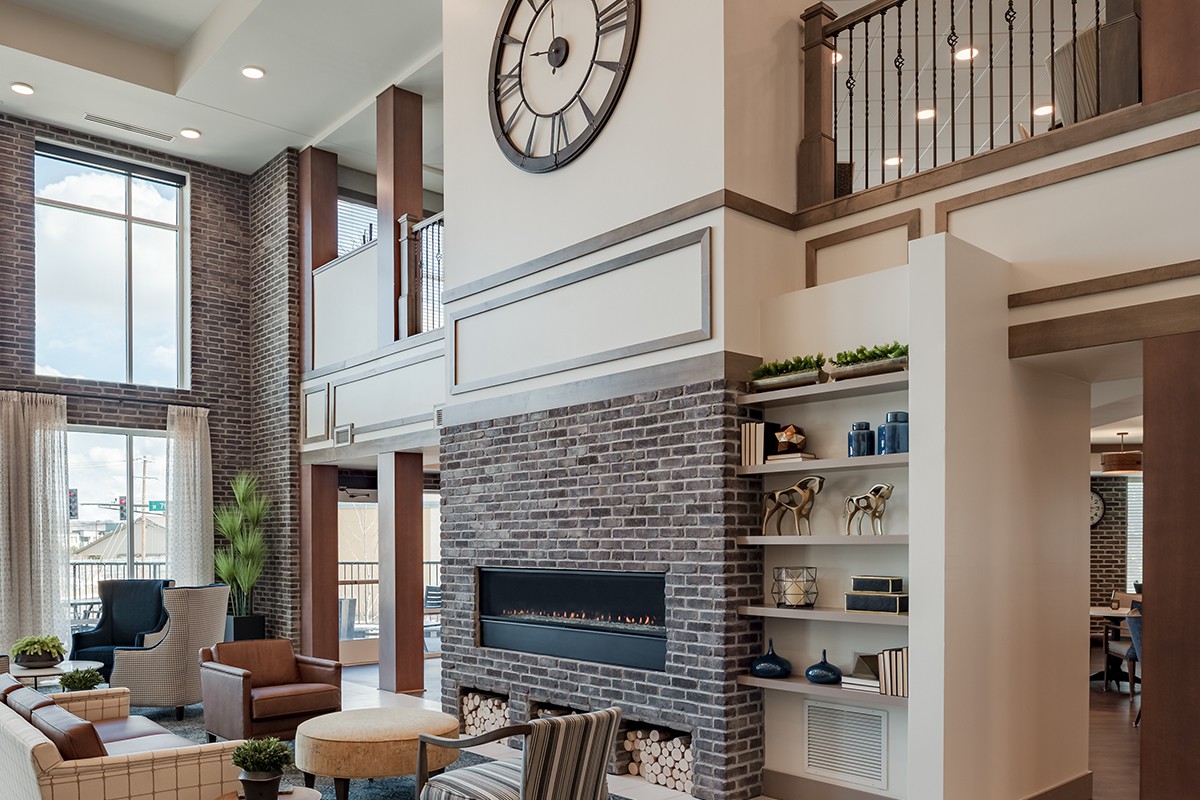 A modern living room with a large clock above a brick fireplace and stylish shelving.