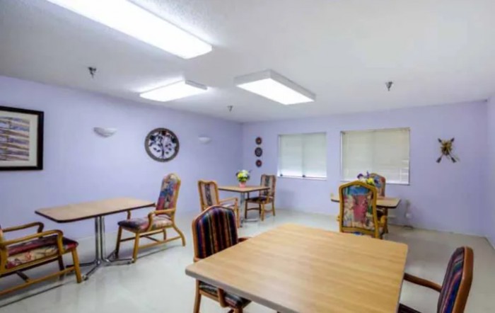 A simple dining room setup with wooden tables and colorful cushioned chairs.