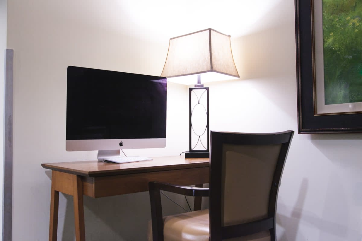 A neatly arranged workspace with a computer, lamp, and chair.