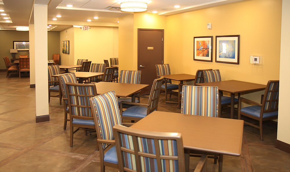 An empty dining area with striped chairs and wooden tables, featuring warm lighting and framed artwork on the walls.