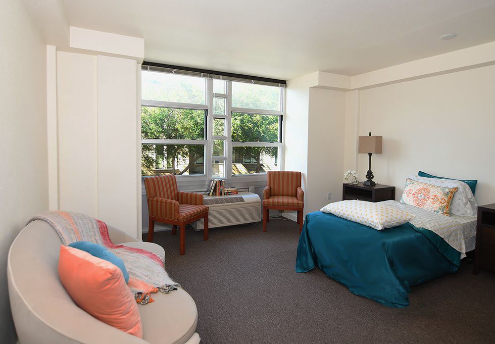 A cozy bedroom with modern furnishings and natural light streaming through a large window.