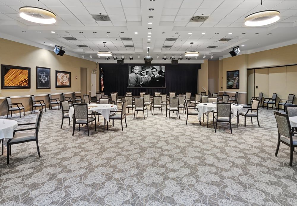 A spacious conference room with neatly arranged tables and chairs facing a stage.