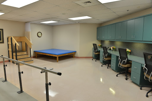 A rehabilitation therapy room featuring a blue exercise mat, support bar, and workstations.
