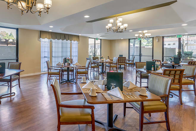 An elegant dining room setup with neatly arranged tables and chairs, illuminated by chandeliers.