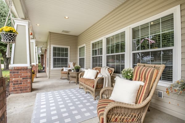 A cozy porch featuring wicker chairs with cushions and a patterned rug.