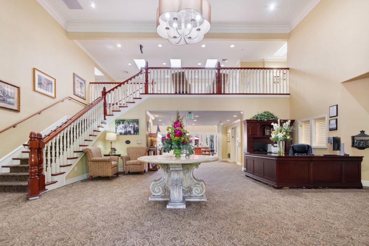 A well-lit lobby featuring a grand staircase, reception desk, and decorative flowers.