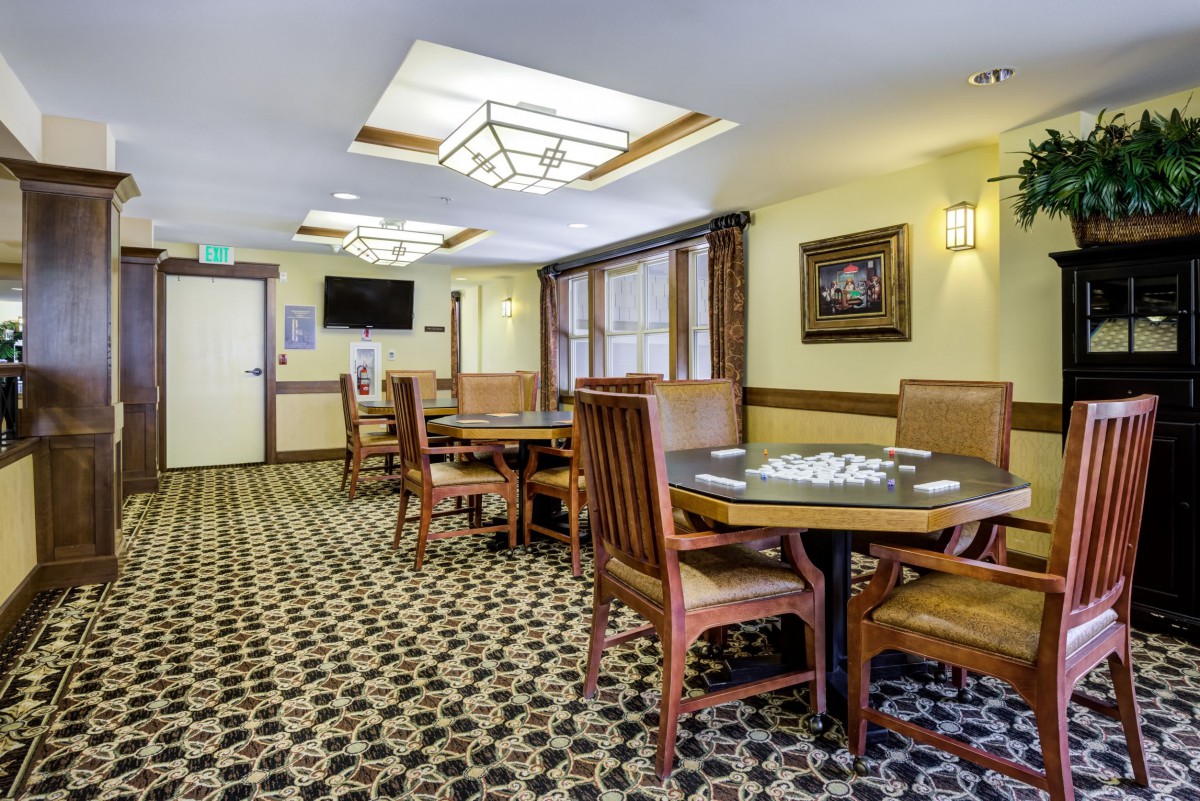 A cozy dining area with wooden tables and chairs, featuring patterned carpet and soft lighting.