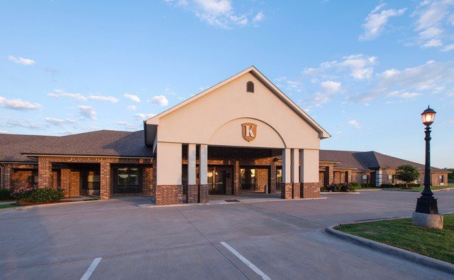 A building with a prominent entrance and parking lot, set against a partly cloudy sky.