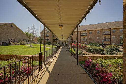 A sunny walkway lined with flowers leading to an apartment complex.