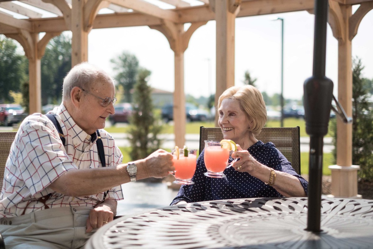 An elderly couple enjoying a refreshing drink outdoors on a sunny day.