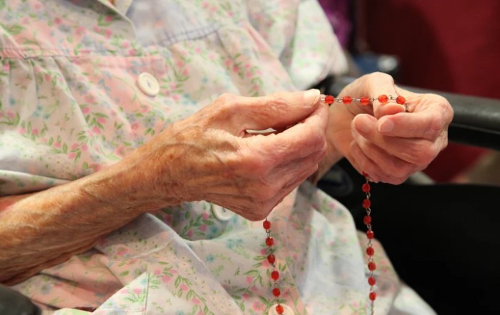 An elderly person holding a rosary, engaged in prayer.