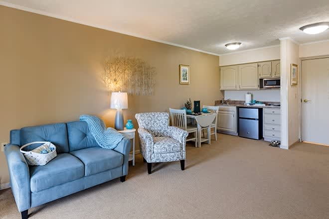 A cozy living space with a blue sofa and patterned armchair adjacent to a small kitchenette.