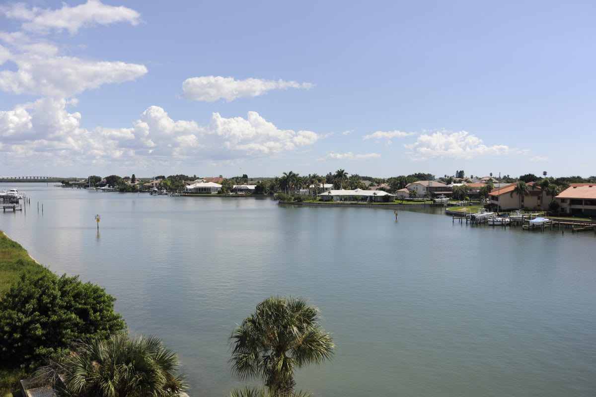 A scenic view of a calm lake surrounded by residential homes under a clear blue sky.