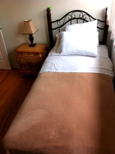 A neatly made single bed next to a nightstand with a lamp.