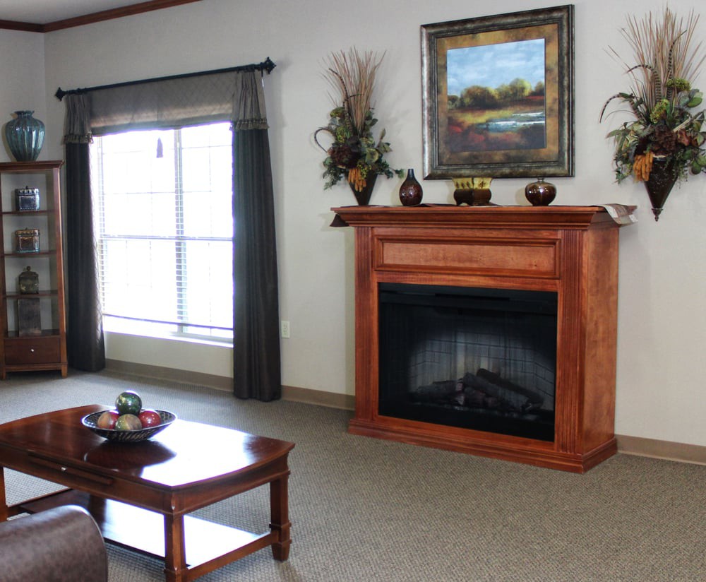 A cozy living room with a wooden fireplace and framed artwork above, featuring comfortable seating and decor.