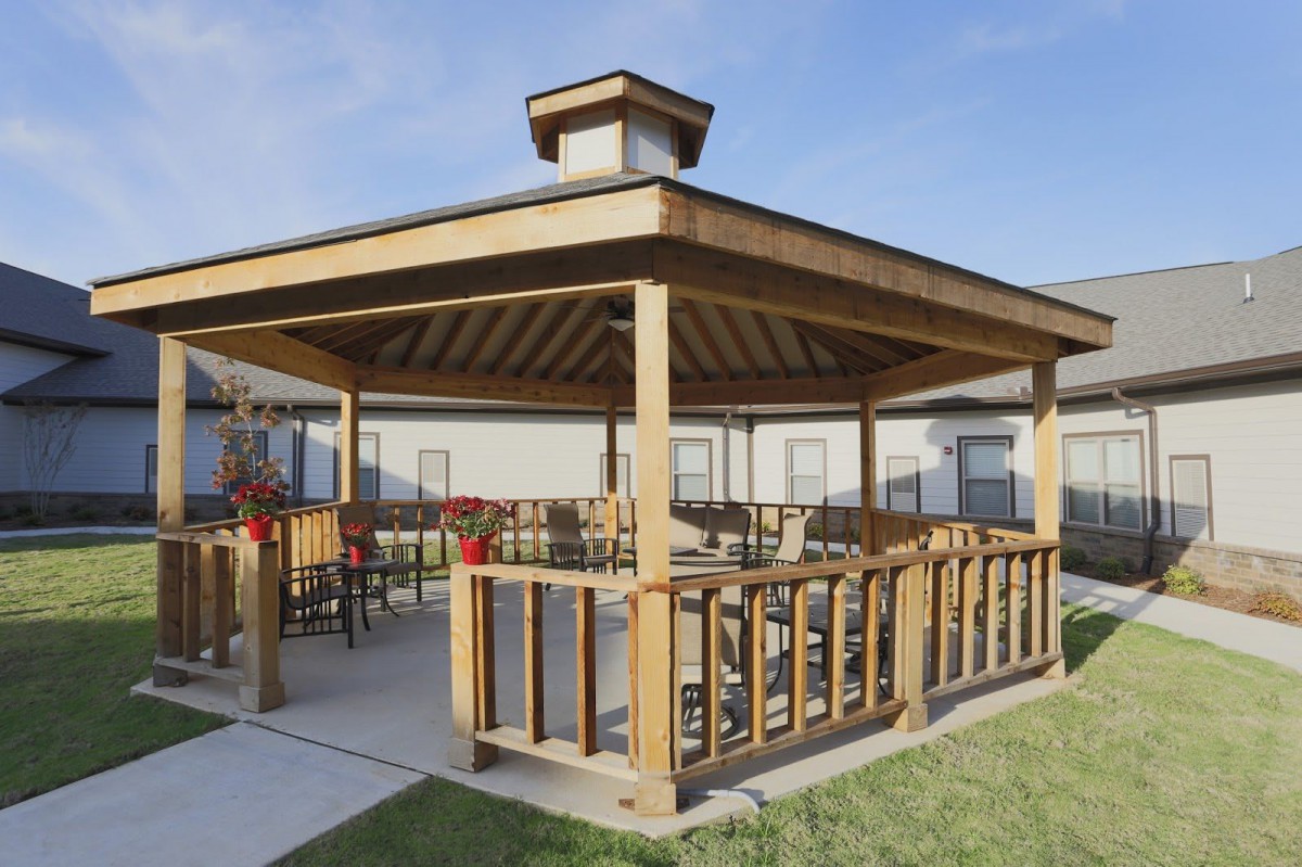A wooden gazebo with seating area, situated in a landscaped outdoor setting.