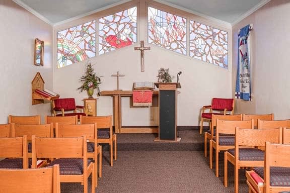 Interior view of a small chapel featuring stained glass windows, wooden pews, and an altar with a pulpit.