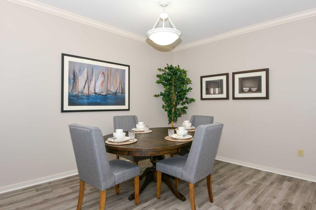 Modern dining room with a round table and gray chairs, adorned with artwork and a potted plant.