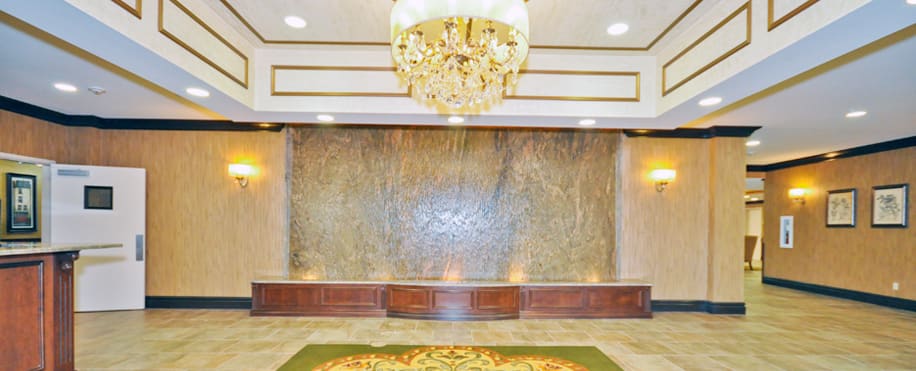 A luxurious lobby with a large chandelier and an elegant water feature against a marble wall.