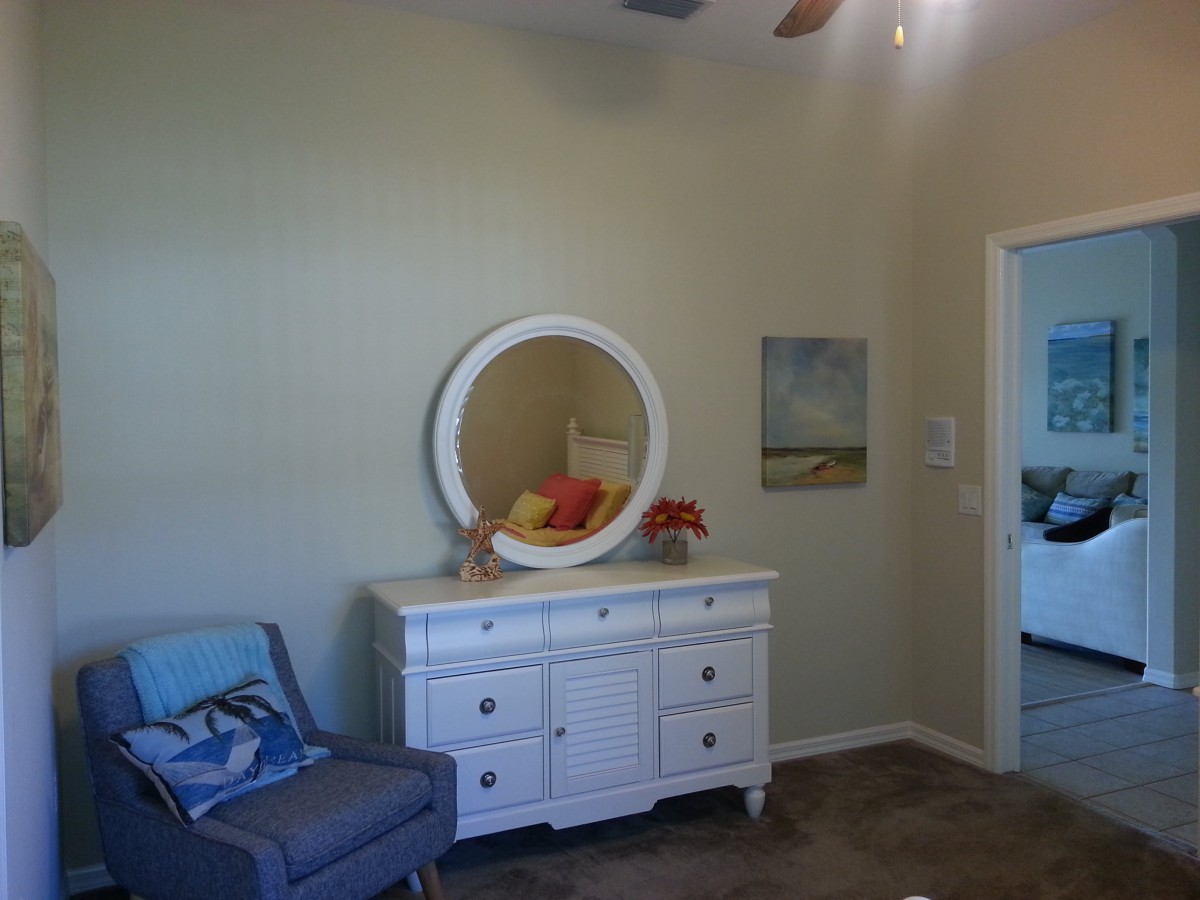 A cozy bedroom corner featuring a white dresser with a round mirror and a blue chair.