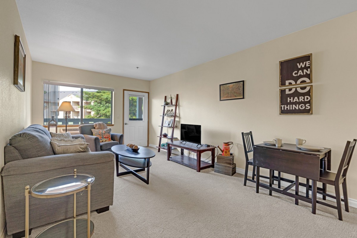 A cozy living room with a sofa, coffee table, TV, dining area, and a window letting in natural light.