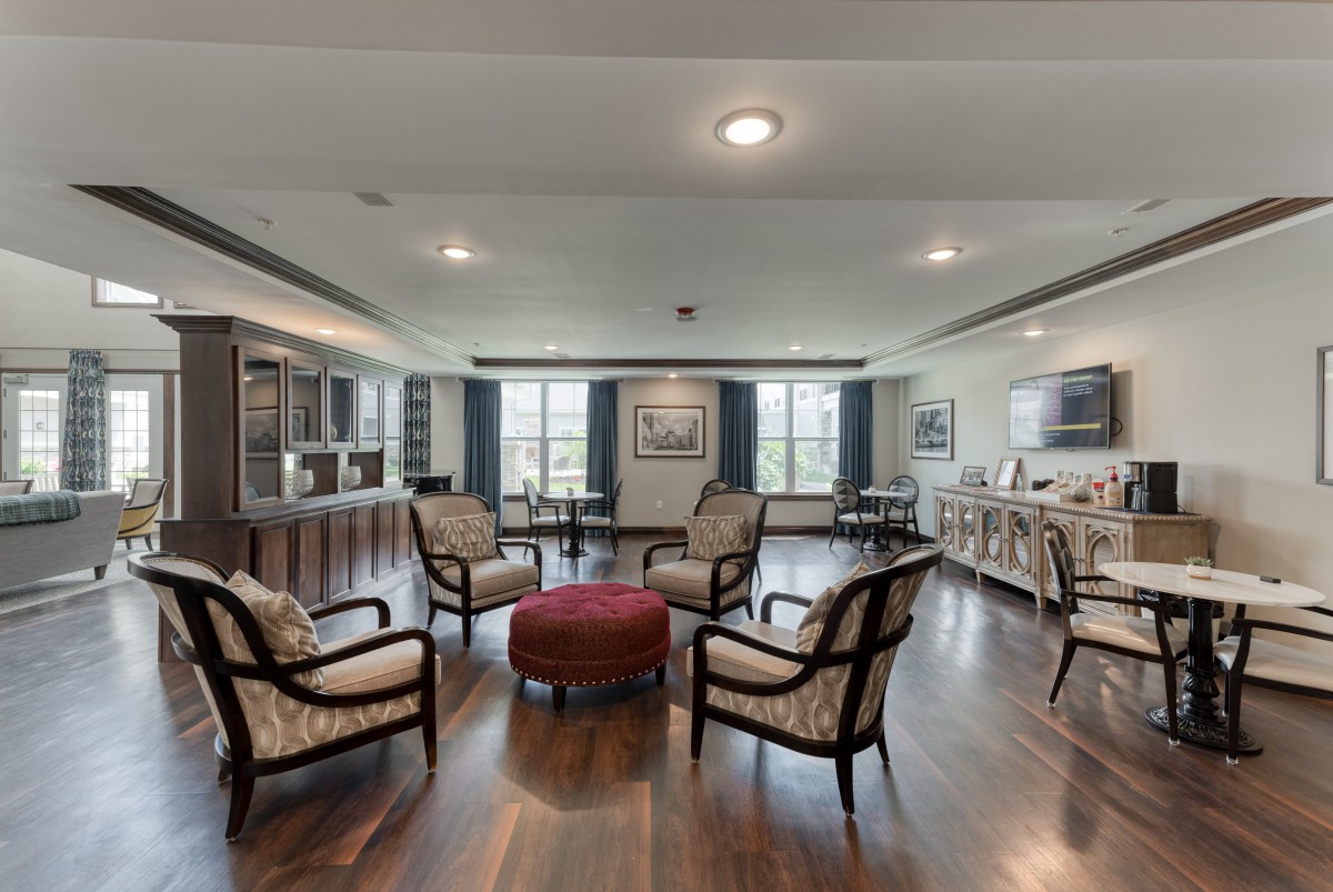 A spacious living room with elegant furniture arranged around a central ottoman and large windows letting in natural light.