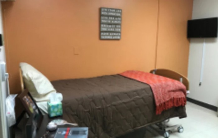 A cozy bedroom with an orange wall and a neatly made single bed featuring a brown bedspread and an orange throw.