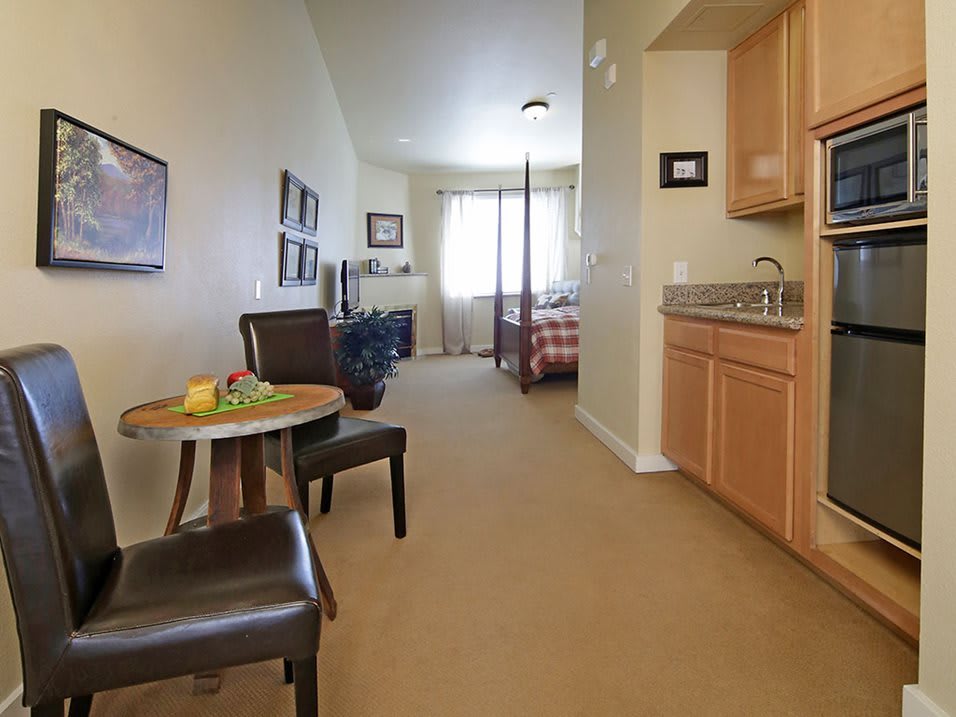 A cozy apartment interior featuring a kitchenette, a small seating area, and a view into the bedroom.