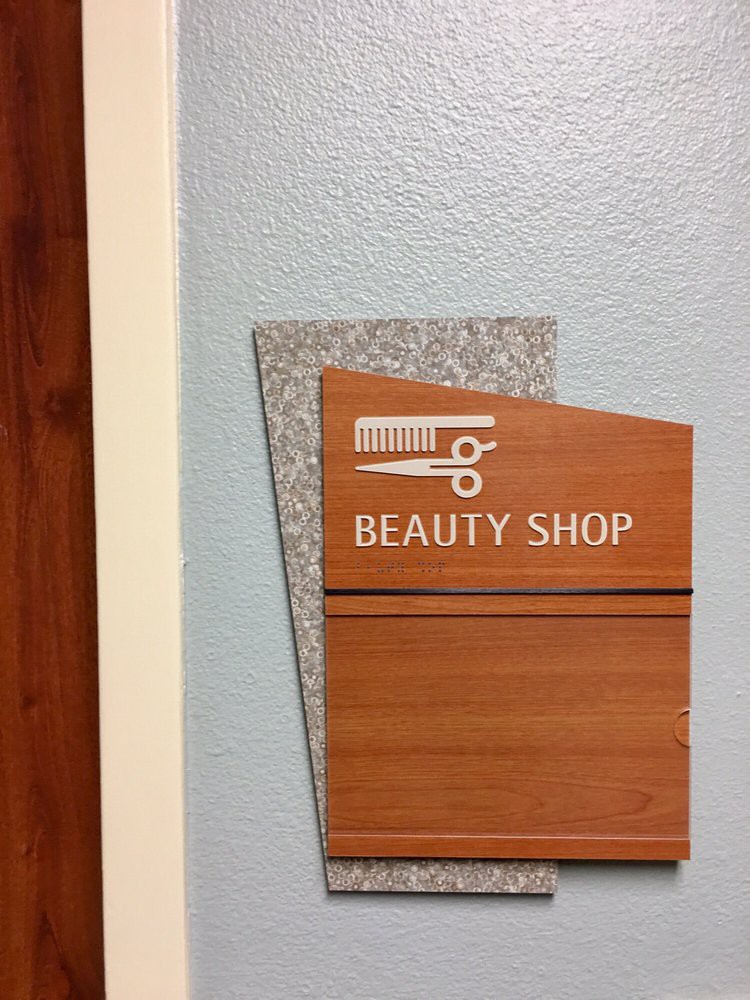 A beauty shop sign with scissors and comb icons on a wall.
