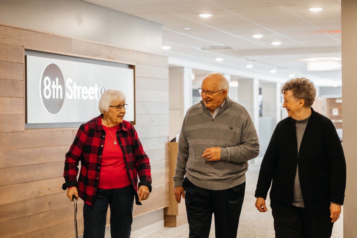 A group of elderly friends walking indoors and having a conversation.