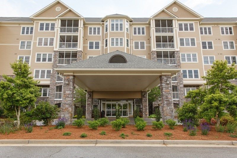 A front view of a multi-story residential building with a covered entrance and landscaped surroundings.