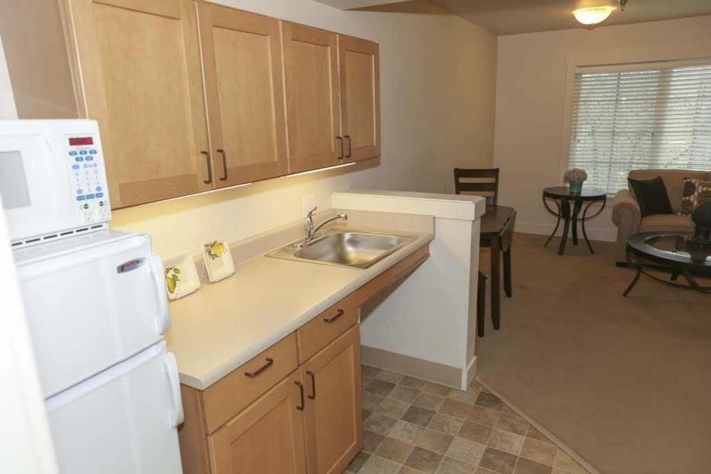 A compact kitchen and dining area in an apartment, featuring wooden cabinets and a countertop with a sink.