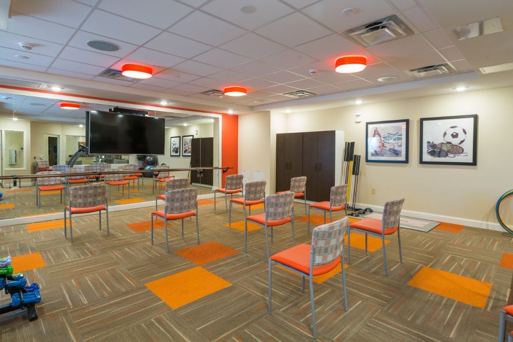 A modern meeting room with orange-accented chairs arranged in a conference setup, featuring a large TV screen.