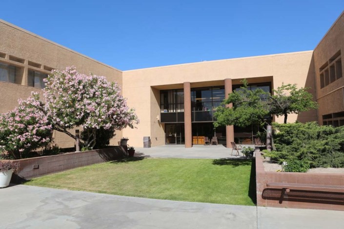 A modern building exterior with a landscaped lawn and trees under a clear blue sky.