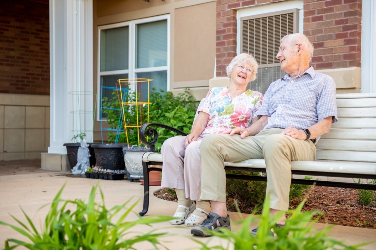 An elderly couple enjoying a moment together on a bench in their garden.
