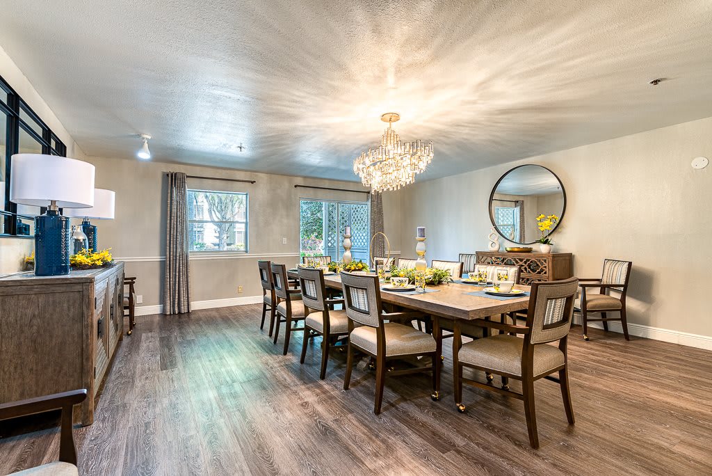 An elegantly designed dining room featuring a large table, multiple chairs, and a stunning chandelier, complemented by wood flooring and tasteful decor.