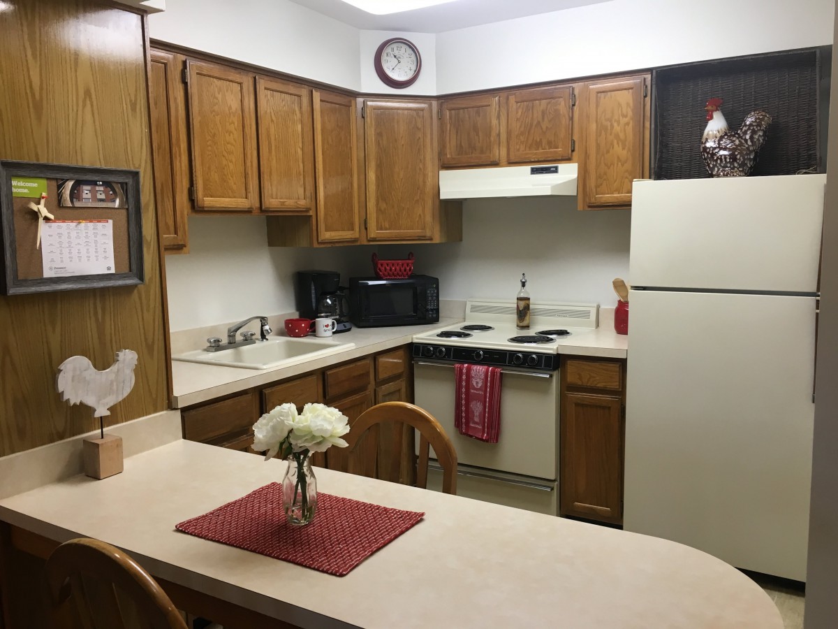 A cozy kitchen with wooden cabinets, appliances, and a countertop adorned with flowers.