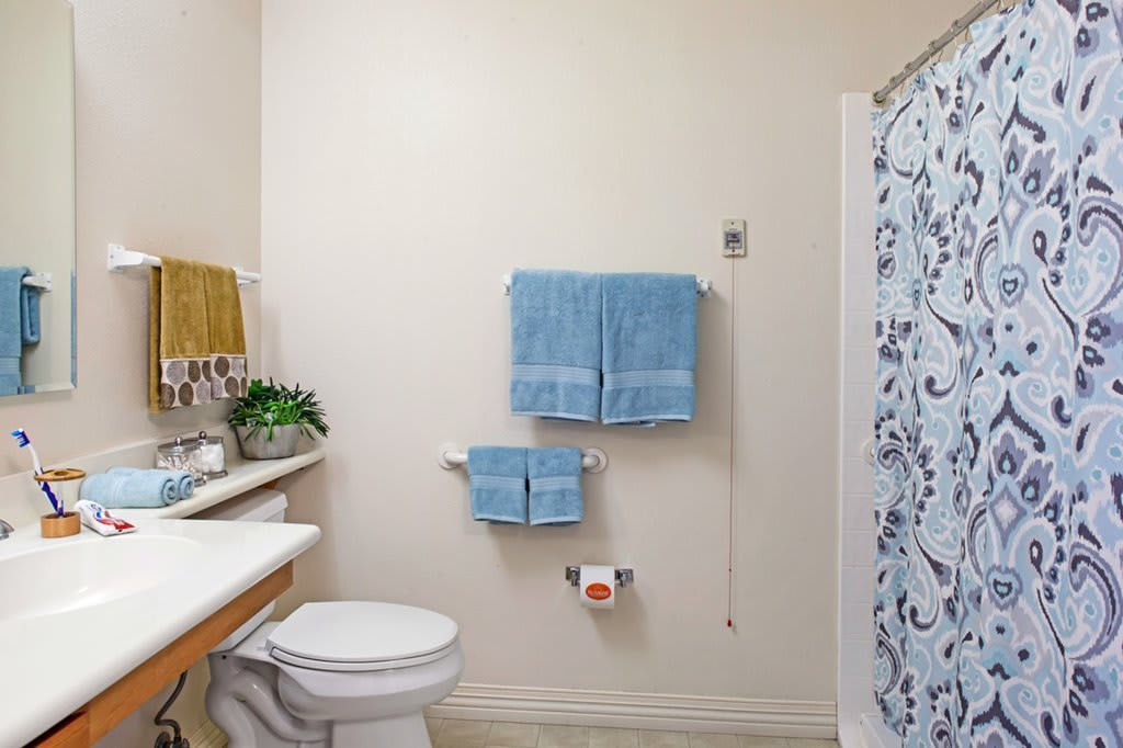 A clean and organized bathroom with a toilet, sink, blue towels, and a floral shower curtain.