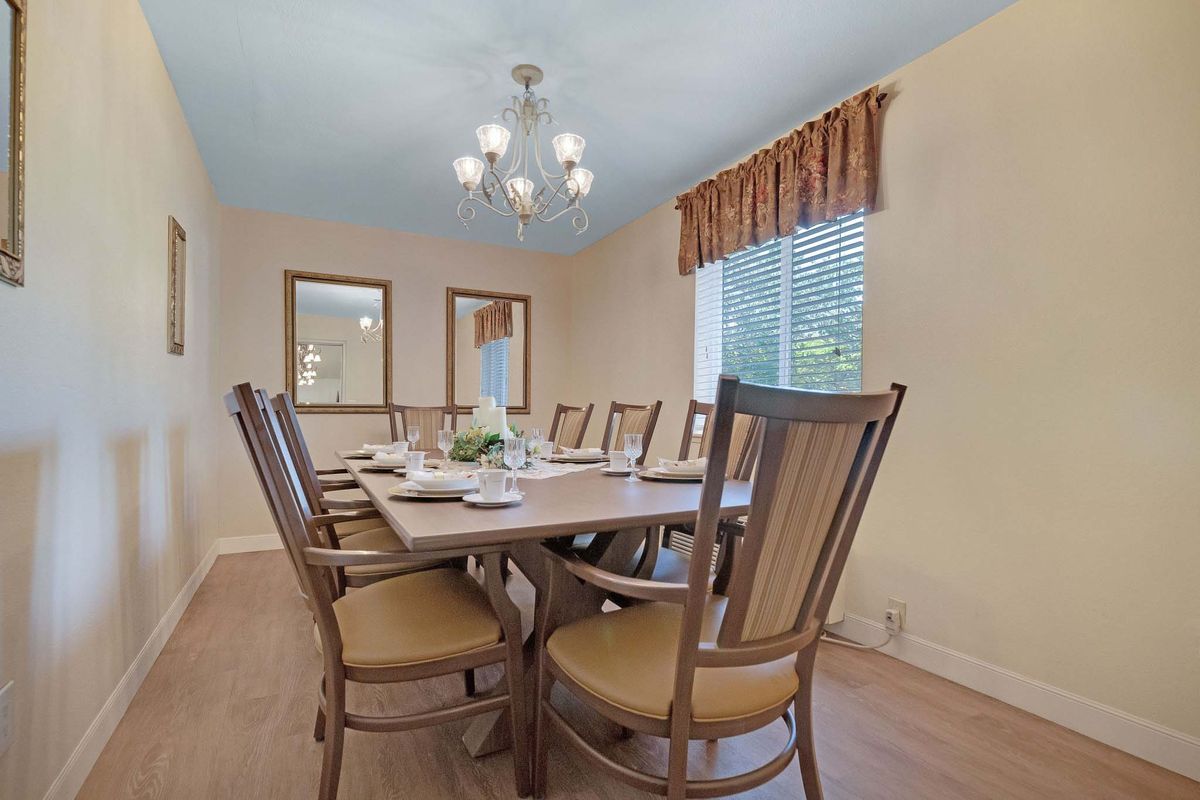 A well-lit dining room with a large table surrounded by wooden chairs, featuring a chandelier and two mirrors on the wall.