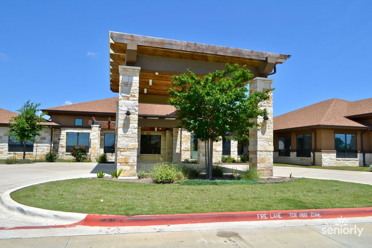 A building entrance featuring stone pillars, surrounded by landscaping and greenery under a clear blue sky.