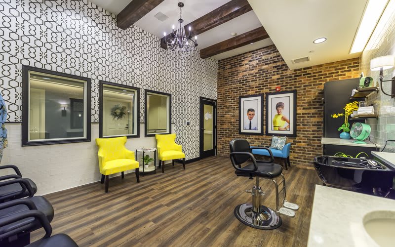 A stylish waiting room with bright yellow chairs, wooden flooring, and a decorative brick wall.