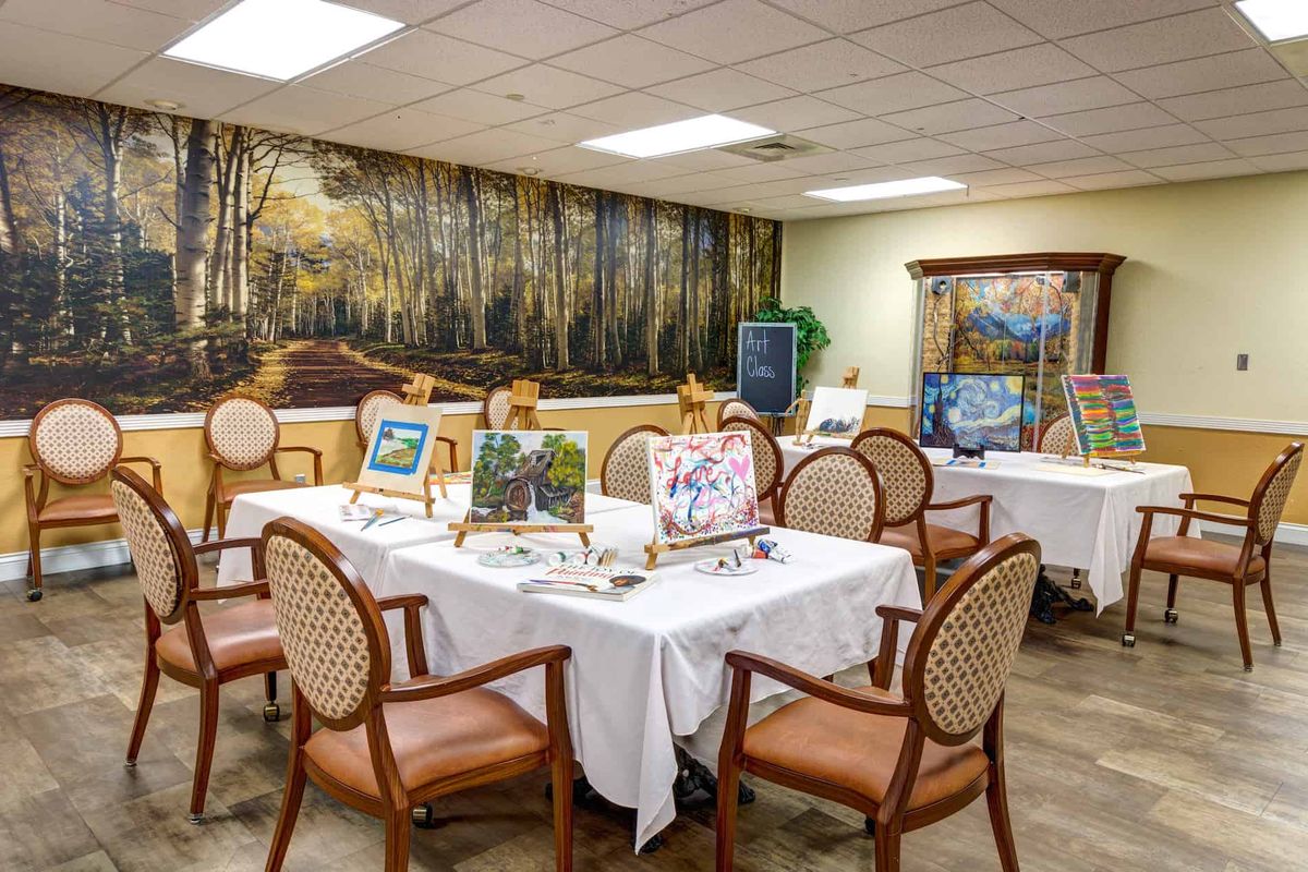 An art exhibition room displaying various paintings on easels and a mural on the wall.