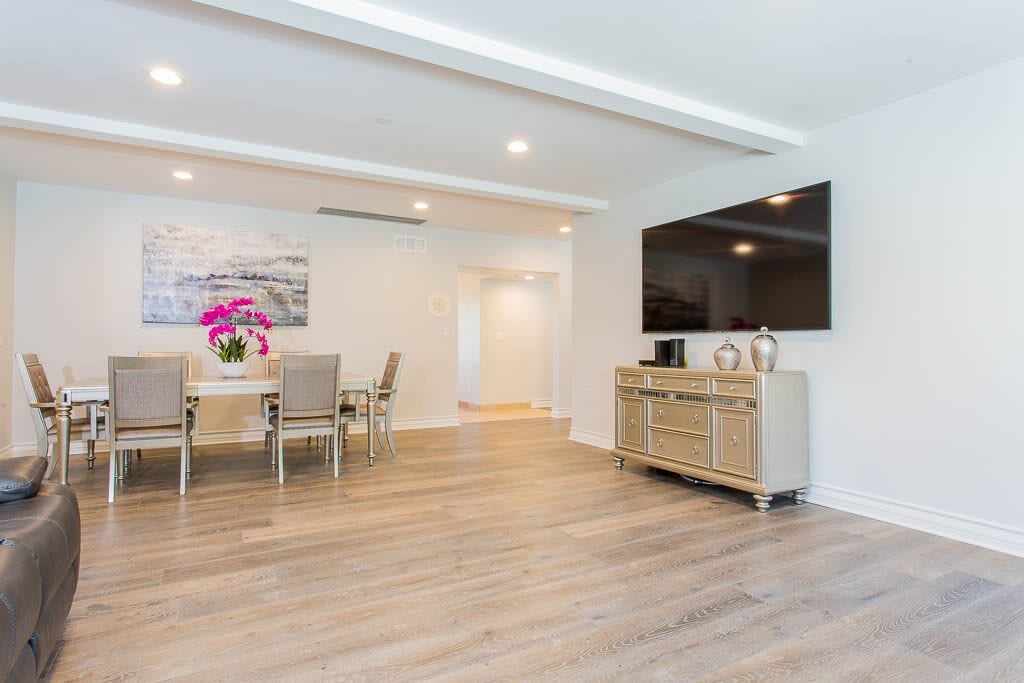 A modern, minimalist living and dining space featuring a large TV, sleek furniture, and hardwood floors.